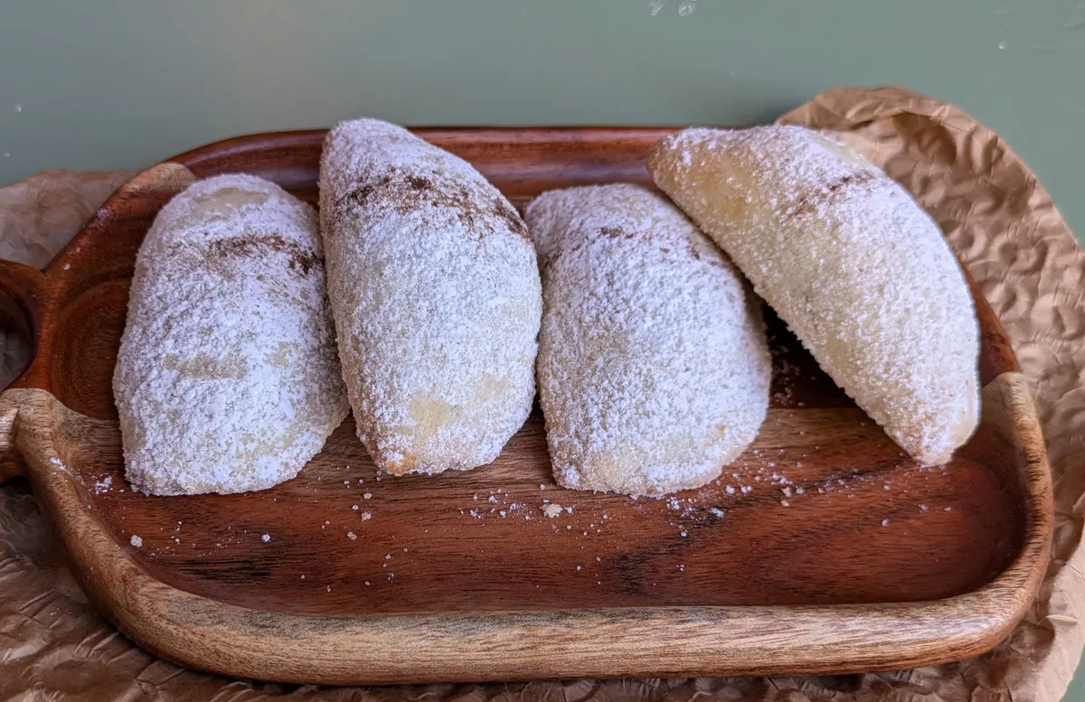 Quattro cassatelle di Agira spolverate di zucchero a velo su un vassoio di legno.